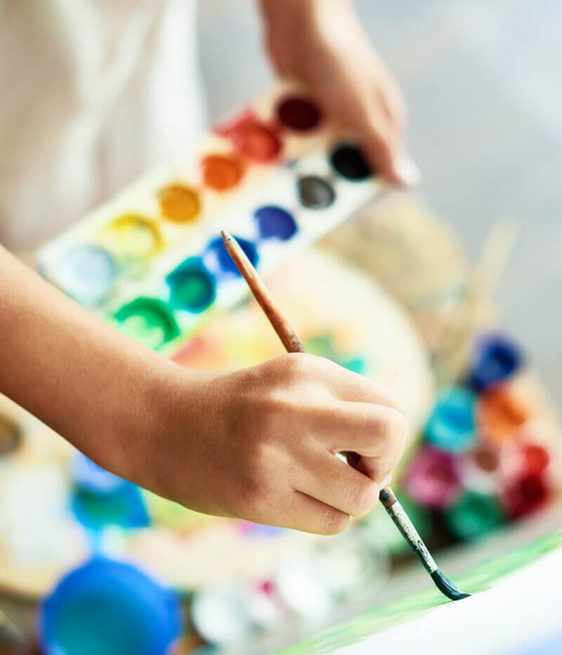 Barn som håller i en pensel och målar med vattenfärger