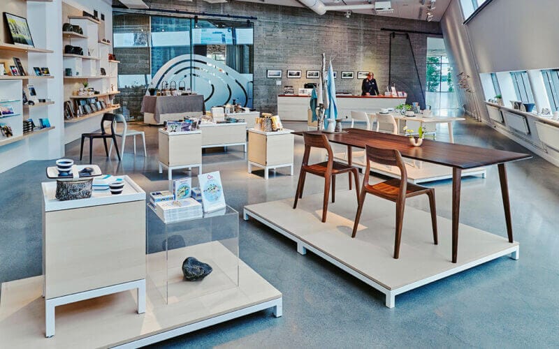 Den moderna konsthallens butiksinredning, med bord, stolar, böcker och olika prydnadsföremål, förvandlas under Artipelagskvällar. När skymningen närmar sig fångar stora fönster till höger det förtrollande naturliga ljuset som förhöjer din upplevelse av Artipelags kvällsevenemang.
