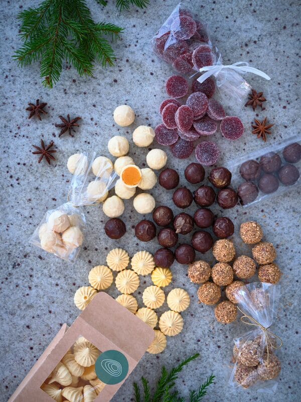 Bild på julgodis som ramlar ur sina kartonger och påsar. I bild syns ljusa- och mörka chokladpraliner, gelehallon och saffransmaränger.