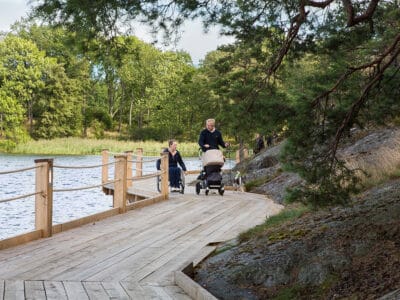 Kvinna i rullstol och man med barnvagn färdas på Artipelags strandpromenad.