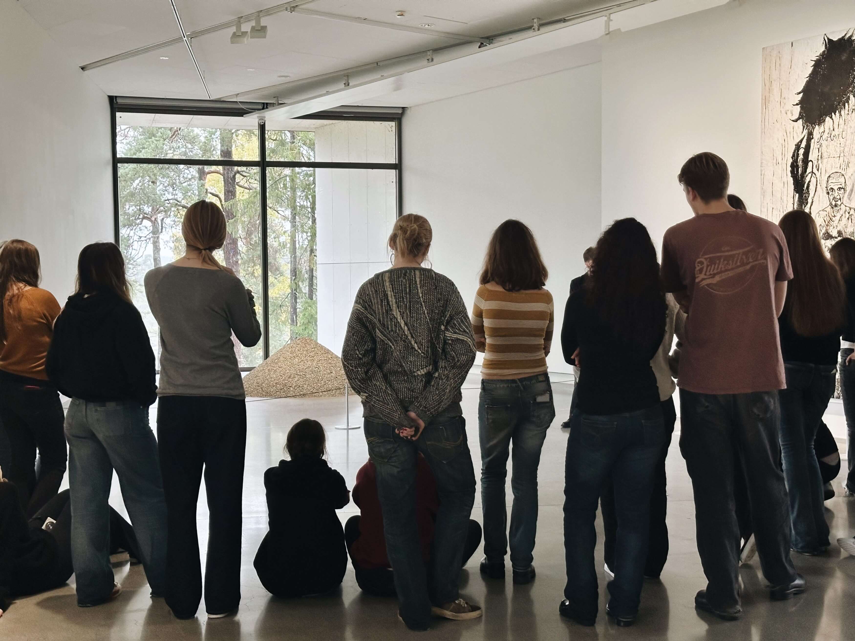 En skolklass står framför ett konstverk i en konsthall under en guidad visning och lyssnar på en guide.