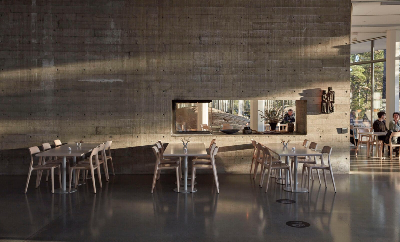 Artipelags moderna interiör har betongväggar. Bord och stolar är placerade framför betongväggen.