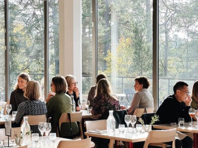 Folk njuter av en Art'n-brunch i den ljusa, moderna restaurangen med stora fönster med fridfull skogsutsikt, som erbjuder både konstupplevelse och läcker brunch.