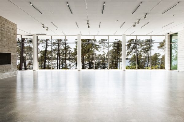 Ett rymligt, tomt rum på Om Artipelag har stora fönster från golv till tak som ramar in höga träd och ett avlägset vatten. Det polerade betonggolvet och moderna taklampor bidrar till dess moderna charm.