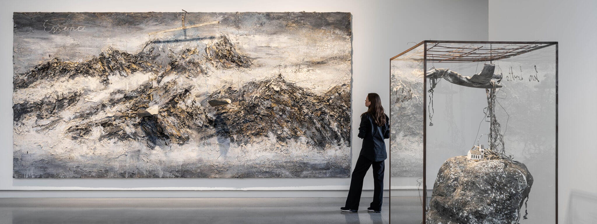 En person använder sitt Art.Pass för att beundra en stor, strukturerad bergsmålning och en skulptur inkapslad i en glasmonter i konsthallen.