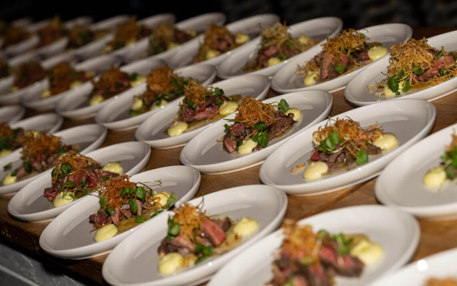 Rader av gourmetbifftallrikar, prydda med stekt lök, grönt och krämig sås, väntar i förväntan på en träyta. Kan denna utsökta presentation vara en utmanare till Arrow Innovation Awards 2024?.