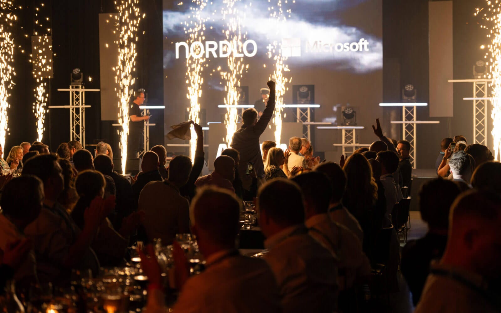 Människor som deltar i Arrow Innovation Awards 2024 i en svagt upplyst lokal med scen, pyroteknik och upplysta logotyper för Nordlo och Microsoft.