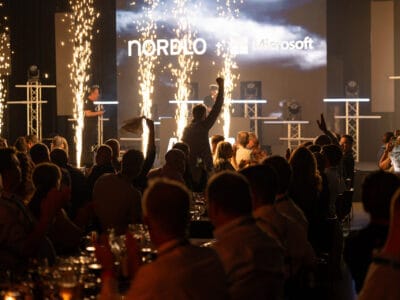 Människor som deltar i Arrow Innovation Awards 2024 i en svagt upplyst lokal med scen, pyroteknik och upplysta logotyper för Nordlo och Microsoft.