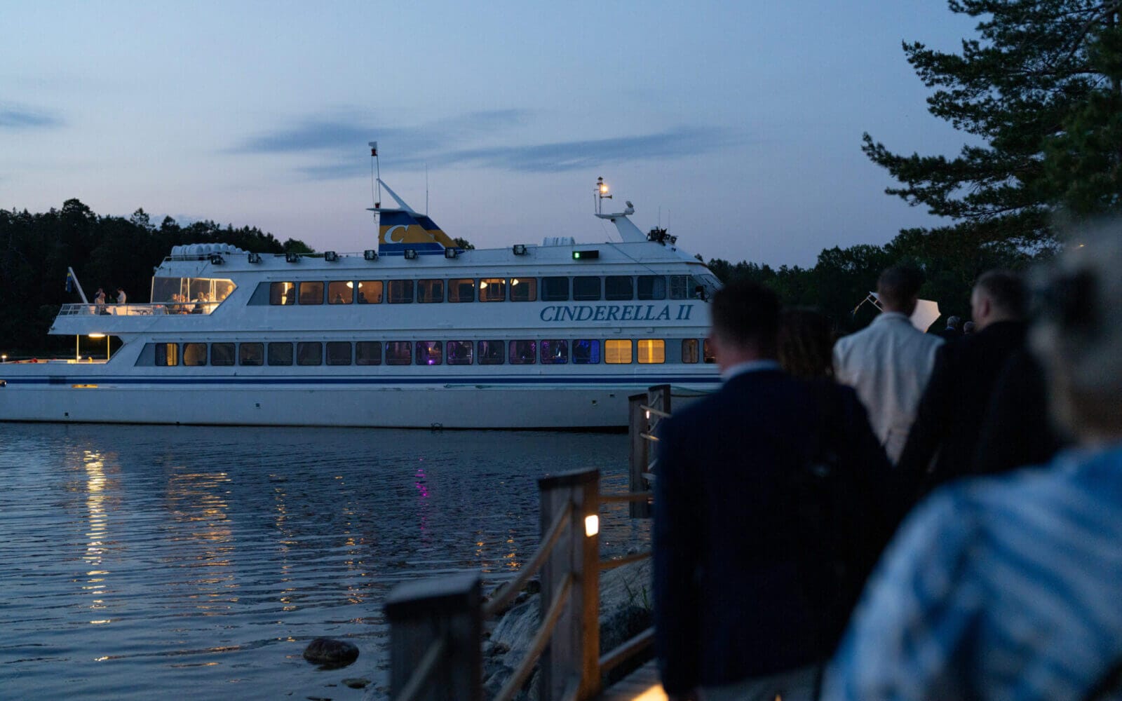 En grupp människor promenerar längs en stig mot den dockade båten "Cinderella II" när skymningen kastar sitt sken, kanske reflekterar över deras senaste prestationer vid Arrow Innovation Awards 2024.