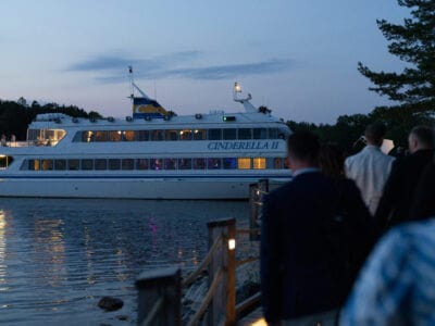 En grupp människor promenerar längs en stig mot den dockade båten "Cinderella II" när skymningen kastar sitt sken, kanske reflekterar över deras senaste prestationer vid Arrow Innovation Awards 2024.