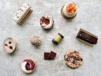 En rad olika bakverk och choklad, konstfullt arrangerade på en strukturerad yta, framkallar den charmiga atmosfären i Bådan Café & Konditori på Värmdö, inbäddat i Stockholms pittoreska skärgård.