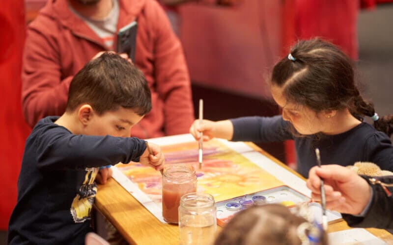 Två barn fokuserade på att måla vid ett bord med penslar och burkar med vatten.