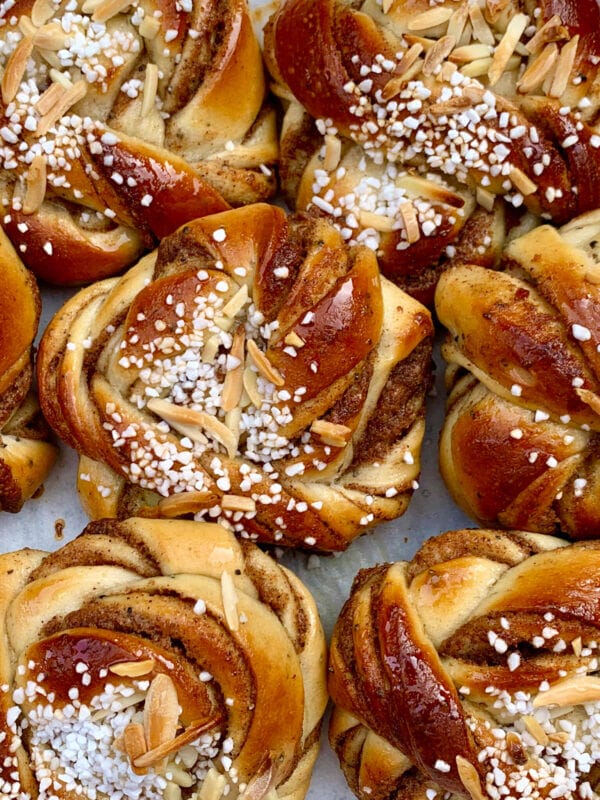 Närbild på flera svenska kanelbullar toppade med pärlsocker och skivad mandel — njut av dem som en del av månadens erbjudande.