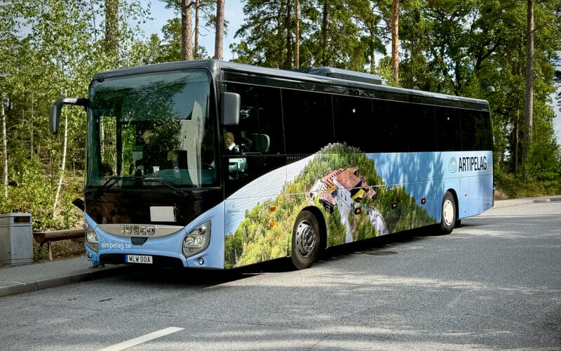 En buss med en ljusblå foliering och en bild över Artipelags byggnad och naturmarker.