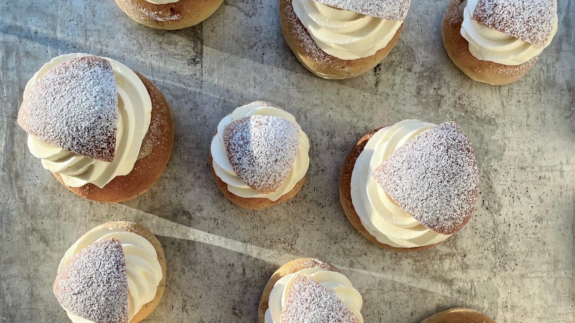 En bild tagen ovanifrån på semlor på en plåt.