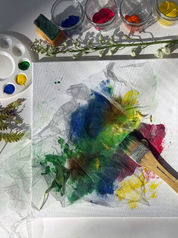 Målarfärg, penslar, växter och en målning som håller på att målas.