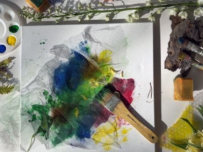 Målarfärg, penslar, växter och en målning som håller på att målas.