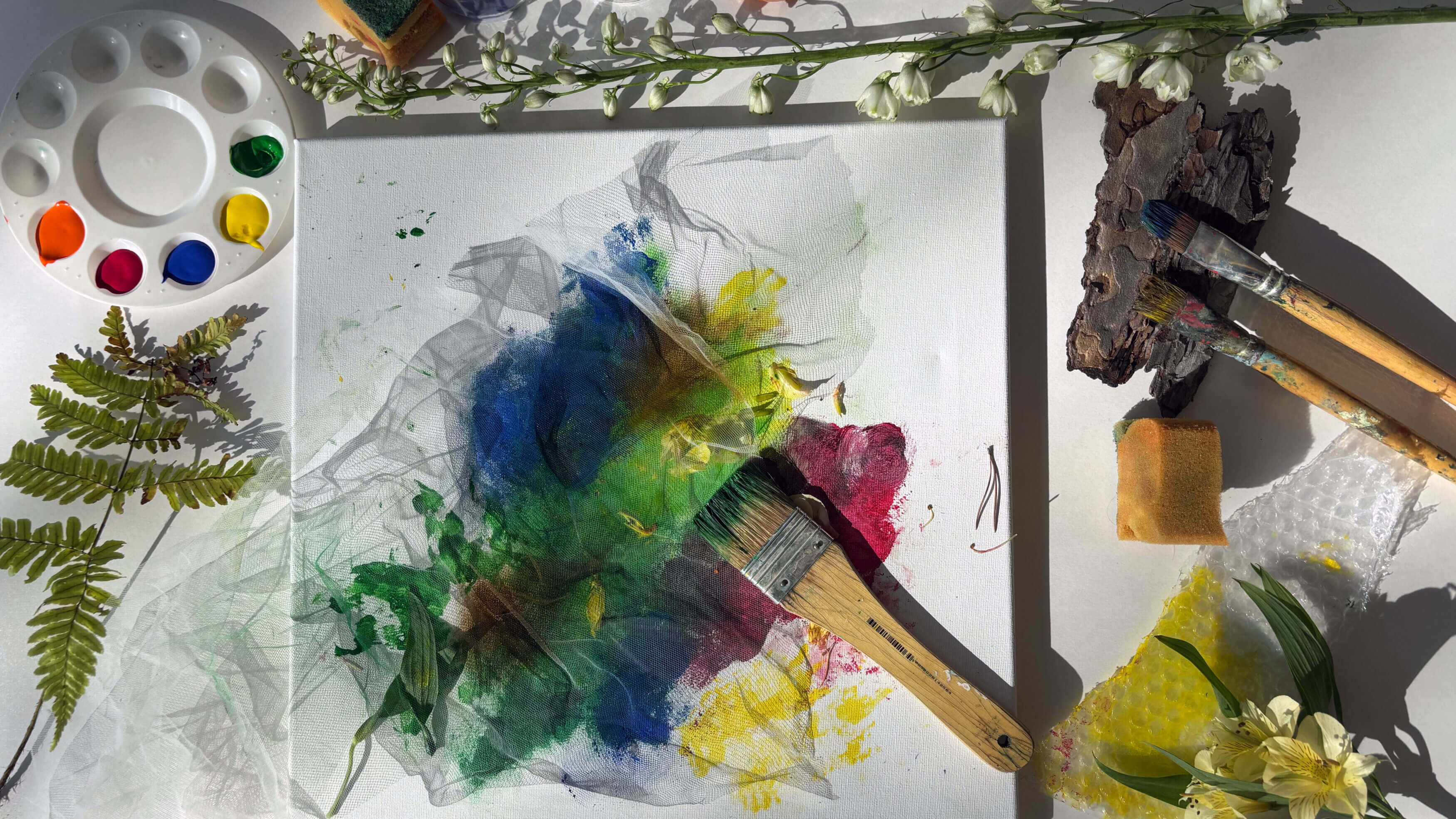 Målarfärg, penslar, växter och en målning som håller på att målas.