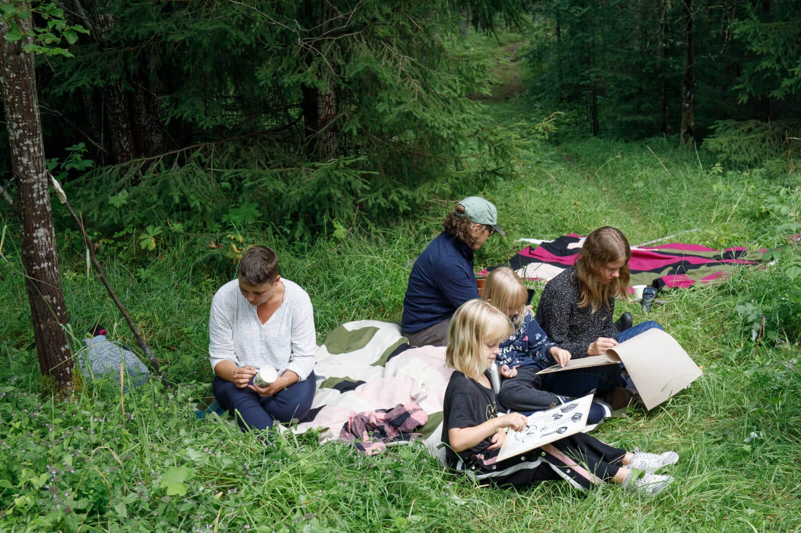 En grupp barn och vuxna som sitter i gräset och ritar.